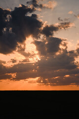 Colorful orange sunset with tree silhouette in the german countryside with fields and panorama horizon views. Dramatic and moody sunset with dark clouds.