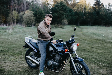 man in a leather brown jacket and a motorcycle in the summer forest, a city motorcycle. motorcyclist biker