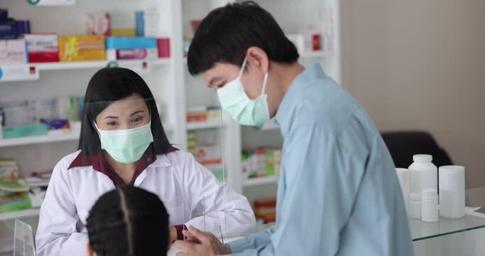 A pharmacist explains the properties of the drug against COVID 19 to his patient, father and daughter. In drugstore Thailand 4K video 