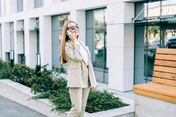 Beautiful business woman talking over the cellphone and walking in urban city street outdoors. Happy lady girl in sunglasses with mobile phone.