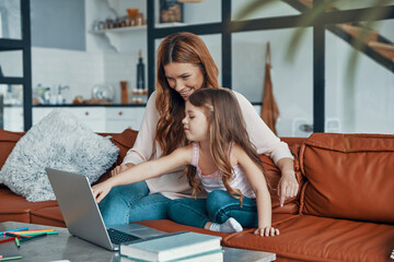 Mother and her daughter bonding together and smiling while using laptop at home