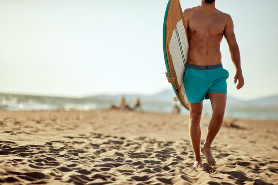 Young handsome male surfer holding a surfboard and walking the beach at sea. Summer, vacation, sea