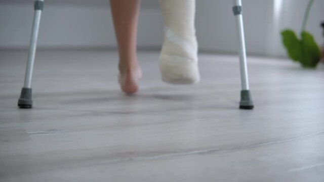 Close-up of woman's broken leg in plaster cast using crutches while walking, rehabilitation after leg injury concept