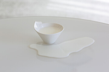 a cup of milk on a white table spilled milk