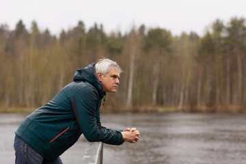 a gray-haired man on a walk in the park by the lake stands on the bridge in spring