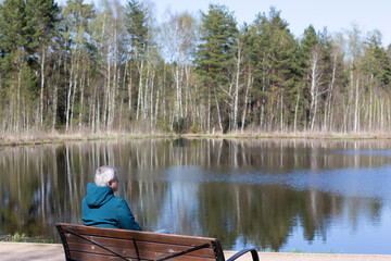 a gray-haired man sits on a bench by the lake in the park