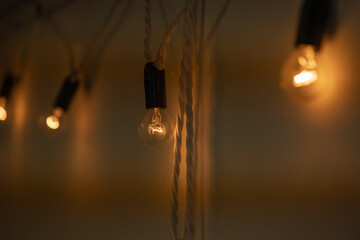 Round small bulbs glowing with warm light hang on a white wall. Loft-style decor. The bulbs are...