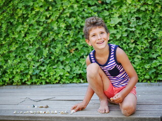 Cute little boy sits on wooden boards in the park and lays out pebbles