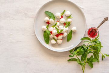 Mozzarella balls with strawberry jam and mint bunch over white background.