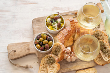 Wine and snacks set. White wine, rustic bread, pickled olives, mozarella cheese over wooden background.