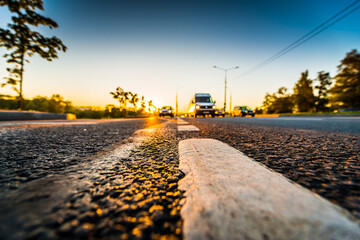 Sunset after rain, the headlights of the approaching cars on the highway. Wide angle view of a close-up from the level of the dividing line