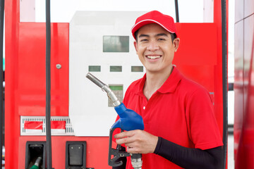 Asian gas station attendant in red uniform stand smiling, holding gas pump nozzle at the gas...