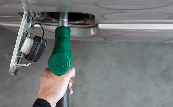 Gas station worker filling up bronze pickup truck tank (Top View). Closeup hand holding green gas pump nozzle.