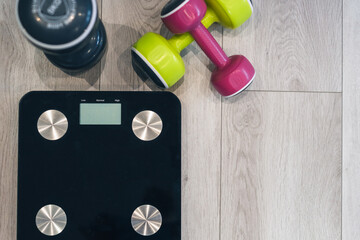 COLOURED DUMBBELLS ON THE WHITE FLOOR OF THE HALL AND BLACK SCALE