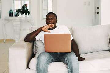 man of african appearance at home on the couch with a laptop chatting