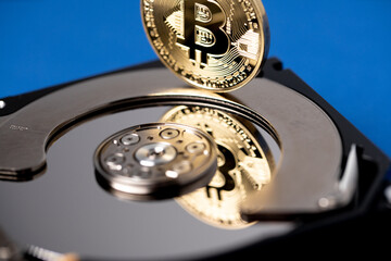 Bitcoin reflecting on hard drive platter. Digital technology and blockchain concept. Gold bitcoin on top of HDD.