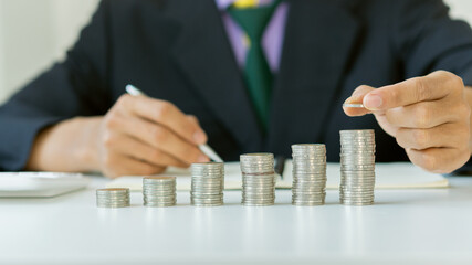 A young businessman puts a pile of coins on his desk, leading the way in calculating and planning finances for savings.