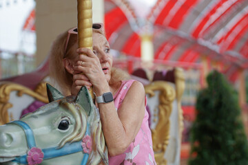 Portrait of Caucasian senior woman ride horse on Carousel at amusement park with lonely mood. Happy living after retirement concept