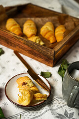 Several butter croissant in a wooden tray on a white table cloth and several jars with jam and butter spread, breakfast