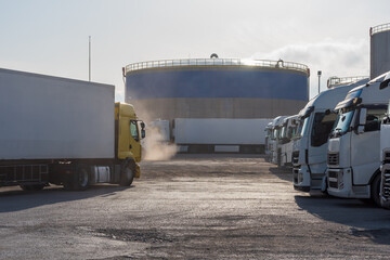 Dirt parking for trucks with a large fuel tank in the background.