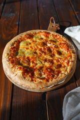 A big round pizza with cheese and tomato sauce on a dark wooden table