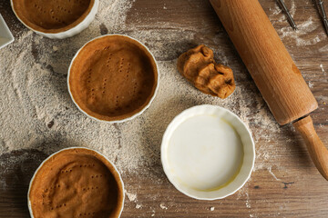 Several small baking forms with dough, flour and rolling pin on a kitchen table