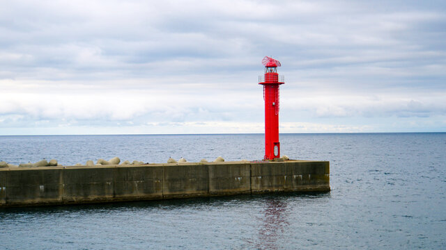 海に突き出た突堤に立つ赤い灯台