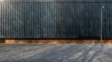 black corrugated sheet metal aluminum facade and concrete wall of a warehouse and a cobblestone...