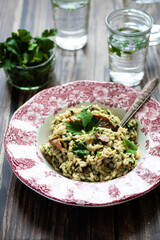 Vegetarian barley risotto with roasted mushrooms, coriander in plat. Glasses water and coriander in glass boll. 