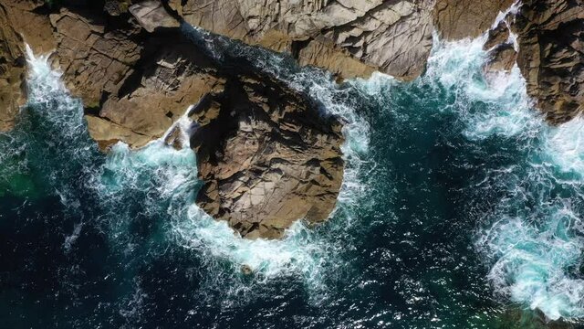 Vue a&eacute;rienne de drone de vagues s'&eacute;crasant avec force sur des rochers en Corse. Vue de dessus montant progressivement des fonds limpides de la M&eacute;diterran&eacute;e