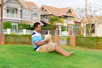 Happy Asian man playing with brown Pug in garden
