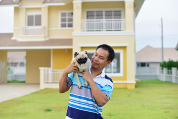 Happy Asian man playing with brown Pug in garden