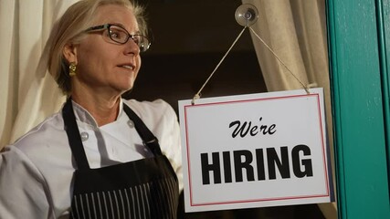 Female shop owner putting Help Wanted sign on glass door. Woman staff chef of restaurant advertising for hiring staff.
