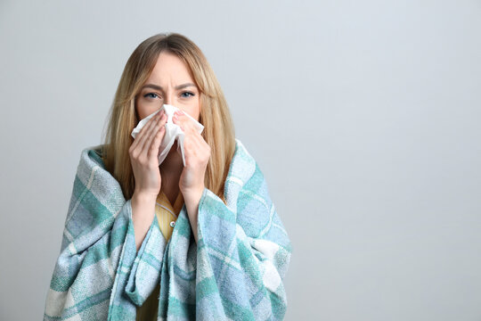 Young woman with blanket suffering from runny nose on light background. Space for text