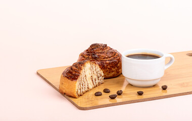 White cup with black coffee and cinnamon rolls on a cutting board.