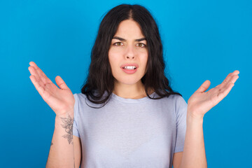 Indignant young beautiful tattooed girl wearing blue t-shirt standing against blue background...