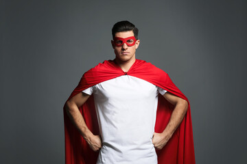 Man wearing superhero cape and mask on grey background