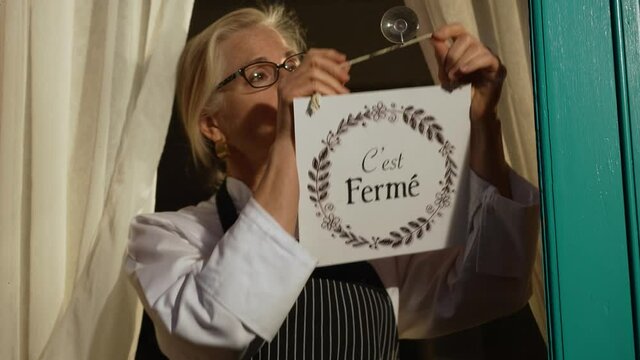 Female shop owner turning ouvert ferme sign on french cafe glass door. Woman staff chef of restaurant turning open closed sign in french.