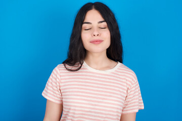 Fototapeta premium young beautiful tattooed girl wearing pink striped t-shirt standing against blue background nice-looking sweet charming cute attractive lovely winsome sweet peaceful closed eyes