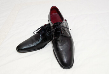 Pair of shiny and stylish textured men's shoes on a white fabric surface.