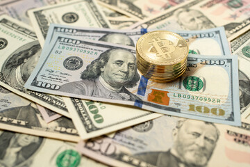 Bitcoin piled up on dollar banknotes. Gold coins on top of one hundred dollar bills. Spread out banknotes as background.