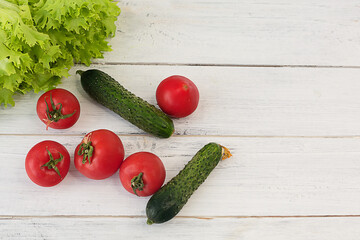 Vegetables tomatoes and cucumbers and salad on a white wooden background.