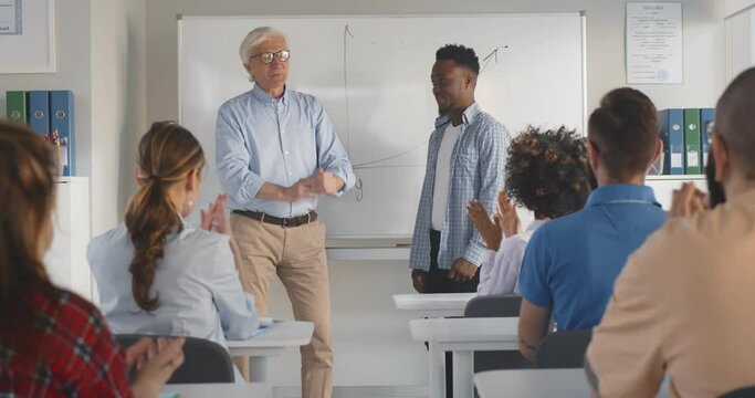 Diverse students group applauding to african classmate standing near white board with professor