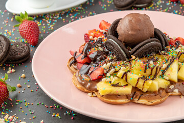 Heart waffle with pineapple and strawberry with gummy candy and ice cream on it.