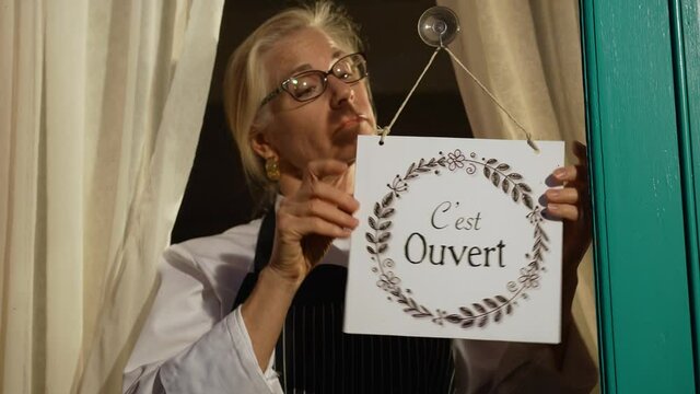 Female shop owner turning ouvert ferme sign in French on cafe glass door. Woman staff chef of restaurant turning open closed sign in French.