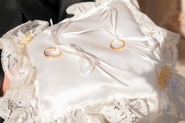 Gold rings placed on a white fabric cushion illuminated by sunlight.