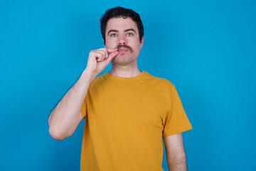 young handsome Caucasian man with moustache wearing orange t-shirt against blue background mouth...