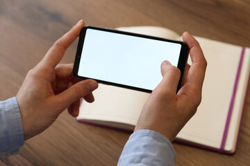 Woman using smartphone with blank screen at wooden table, closeup. Space for text