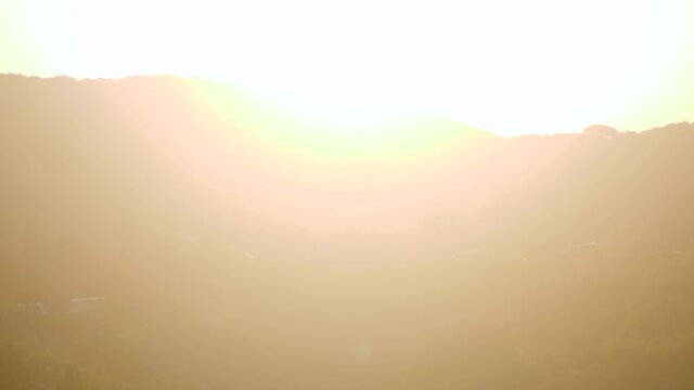 Slow motion shot of young caucasian man looking at hills with the sun making lens flares in camera - pan right