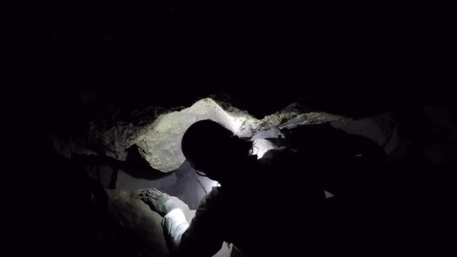 Cave spelunker descends into deeper passage through a restriction
